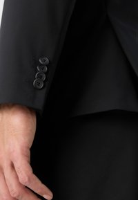 Black blazer cuff featuring four black buttons and narrow stitching details. Smooth fabric texture with a fitted silhouette.