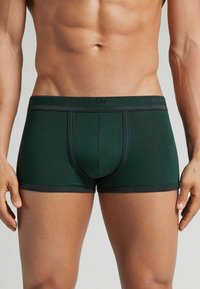 Boxer ajustados de color verde oscuro, hechos de material suave, con una cinturilla elástica negra con marca y un diseño ceñido con costuras en contraste.