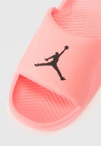 Papuc roz cu talpă slide, finisaj neted și lucios, cu logo negru Jumpman și talpă texturată cu model de tracțiune tip chevron.