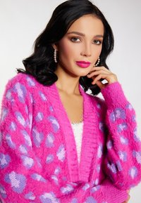 Cárdigan rosa difuso con estampado de leopardo morado, puños acanalados y un diseño de escote en V profundo, superpuesto a una blusa blanca.