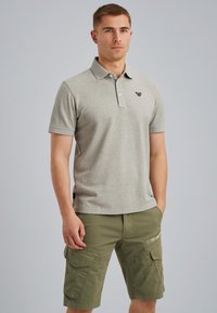 Camisa polo gris claro con cuello, que presenta un pequeño logo oscuro en el pecho, combinada con pantalones cortos cargo de color verde olivo.
