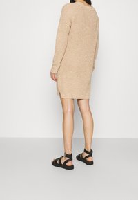 Robe-pull en maille beige à finition texturée, manches longues, coupe décontractée et fentes latérales. Associée à des sandales noires à fines lanières.