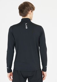 Sort langærmet atletisk top med høj krave, fugttransporterende materiale, subtil logo detalje på ryggen og reflekterende detaljer på ærmerne.
