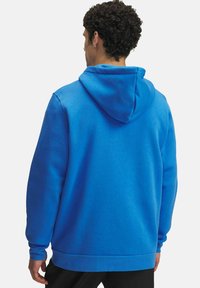 Sudadera de forro polar azul con capucha ajustable, puños y dobladillo acanalados; presenta una textura suave y un ajuste relajado, vista desde la parte posterior.