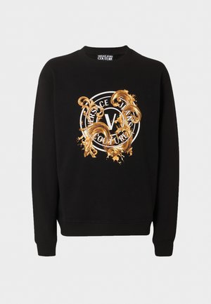 Svart genser med rund hals, med gullfarget dekorativt mønster og hvit rund logo med teksten "Versace Jeans Couture" på forsiden.