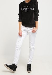 Sudadera de terciopelo negro con el texto "HOY TE VES HERMOSA" , combinada con jeans skinny blancos y zapatillas negras de caña alta.