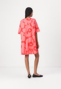 Short-sleeve pink floral dress with a relaxed fit, featuring large red and light pink flower patterns. Black flat shoes.