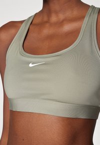 Maslinasto zeleni sportski grudnjak od glatkog, rastezljivog materijala, s okruglim izrezom i malim bijelim Nike logom sprijeda.
