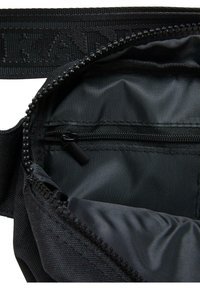 Zwarte nylon tas interieur met een gladde textuur, voorzien van een ritsvak en een dikke schouderband. Naaddetails zijn zichtbaar langs de randen.