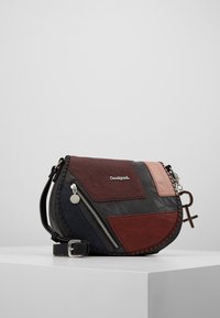 Černá, červená a růžová kožená crossbody taška s zakřiveným tvarem, dekorativním prošíváním, zipovým uzávěrem a připojeným přívěskem.