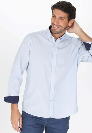 Chemise boutonnée bleu clair à manches longues, avec des poignets contrastants bleu marine et un col classique, fabriquée en tissu coton.