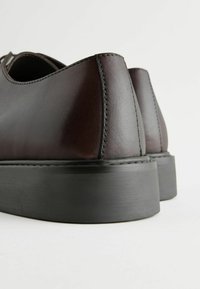 Ruske nahkasaappaat sileällä pinnalla, pyöreällä takana ja paksulla mustalla kumipohjalla. Näkyvät ompeleet reunoilla.