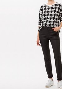 Suéter de patrón houndstooth en blanco y negro combinado con pantalones ajustados negros y zapatillas blancas, creando un atuendo casual y moderno.