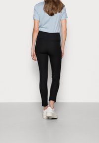 Svarta figurnära byxor med hög midja, med två bakfickor och en slät yta, i kombination med en ljusblå t-shirt och vita sneakers.