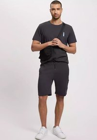 Szary bawełniany zestaw koszulki i szortów, z kieszonką na szortach i małym logo na koszulce. Noszony z białymi trampkami.