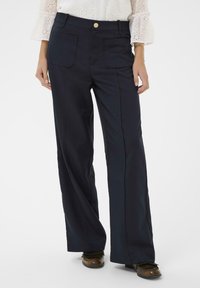 Pantalons larges bleu marine avec deux poches avant, un bouton doré et des lignes épurées. Le tissu semble lisse avec une coupe structurée.