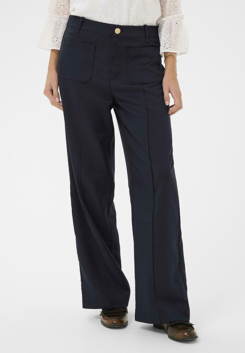 Pantalons larges bleu marine avec deux poches avant, un bouton doré et des lignes épurées. Le tissu semble lisse avec une coupe structurée.