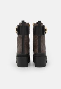 Hnědé kotníkové boty s vzorem a černými koženými akcenty, robustním černým podpatkem a zlatým detailem na bočním sponě.
