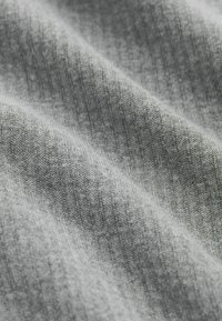 Graues Strickgewebe mit weicher Textur, das dezente Rippungen und verschiedene Schattierungen aufweist, die ein sanftes, ungleichmäßiges Muster erzeugen.