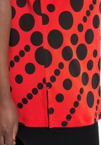 Top corto de manga corta rojo con grandes lunares negros y una abertura lateral. Fabricado en una tela suave y ligera con un corte regular.