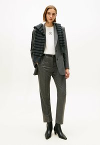 Abito grigio a righe con una vestibilità su misura, caratterizzato da una camicia bianca e una sciarpa in maglia a righe scure cadente sulle spalle. Stivali neri con tacco.