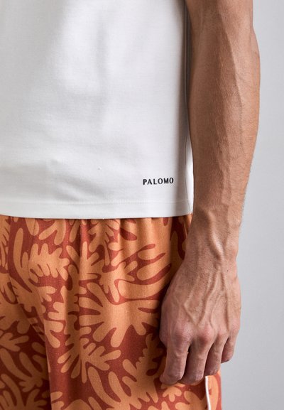 White short-sleeve t-shirt with "PALOMO" printed in black on the lower hem, paired with orange shorts featuring a large leaf pattern.