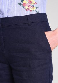 Marinblå linneshorts med skräddarsydd passform, med sidofickor och en mjuk yta, delvis synliga tillsammans med en randig blå blus.