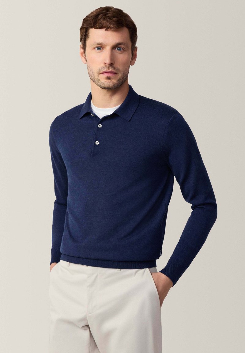 Granatowy, długi sweter polo z kołnierzykiem, trzema guzikami i fakturowanym splotem. W połączeniu z jasnymi spodniami.