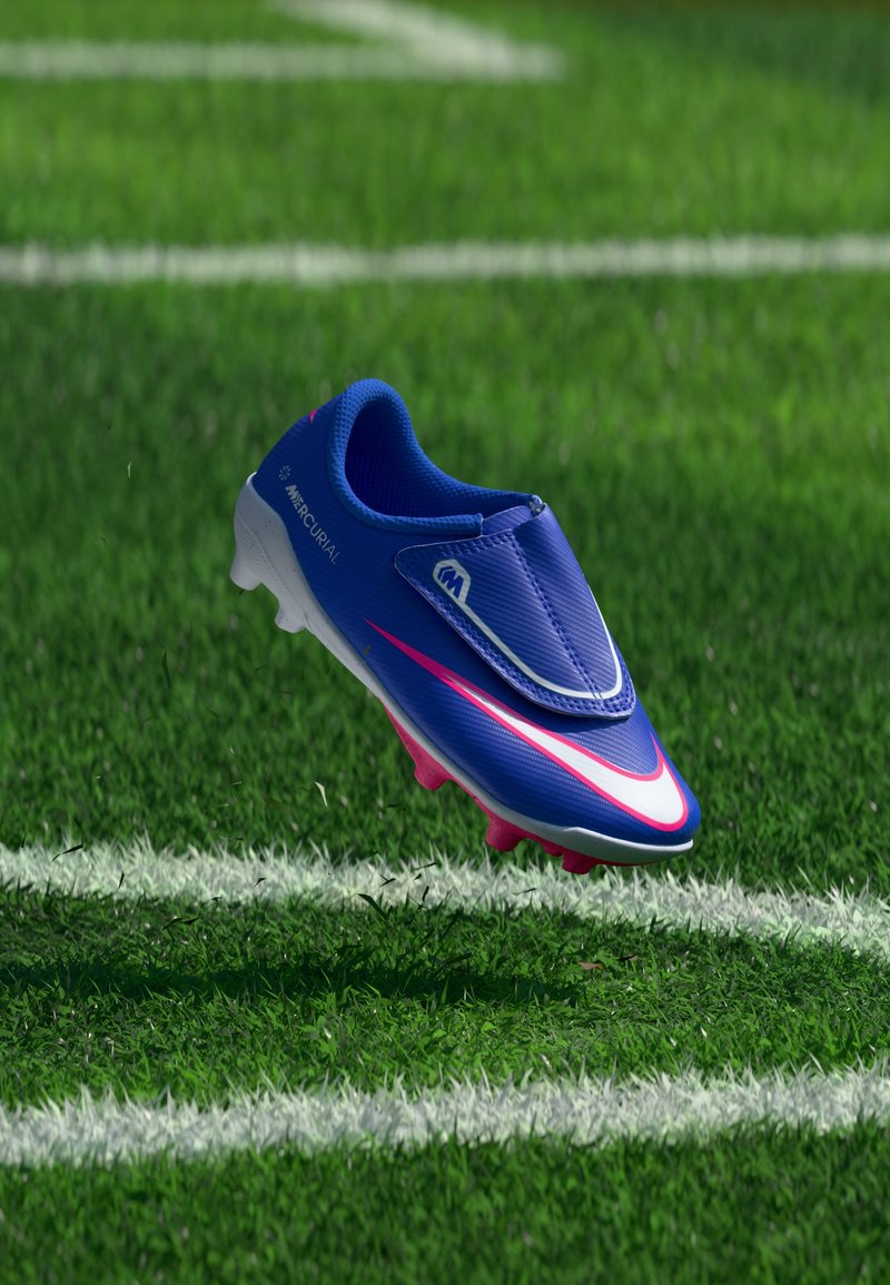 Botas de fútbol Nike Mercurial azul y rosa en el aire sobre un campo de césped verde cerca de líneas blancas pintadas.