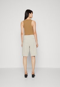 Barna ujjatlan top világos bézs sorttal kombinálva, laza szabással és hátsó zsebekkel. A modellen fekete magassarkú papuccsok vannak.