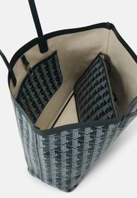 Sac fourre-tout noir et beige avec une pochette intérieure à motif géométrique et un compartiment zippé, doté de fines anses noires.