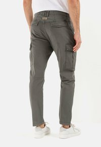 Graue Cargo-Hosen mit schmaler Passform, seitlichen Taschen, glatter Textur und konischem Schnitt, kombiniert mit weißen Turnschuhen.