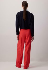 Pull cropped bleu marine à manches longues associé à un pantalon rouge taille haute et à jambes larges. Tissu lisse avec une coupe ajustée.