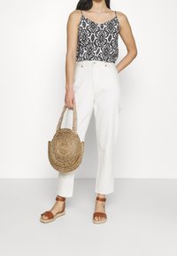 Camisole à motif noir et blanc, pantalon blanc taille haute, sandales marron à lanières et sac rond en paille tressée.