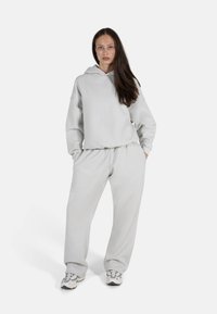 Lys grå hettegenser og matchende joggebukser i et mykt stoff. Hettegenseren har en brystlomme, og buksene har en elastisk midje.