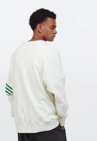 Vit sweatshirt med en lös passform, med gröna ränder på vänster ärm och ribbade ärmslut och fåll. Slät textur, minimalistisk design.