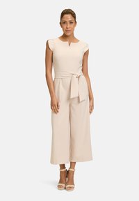 Tuta beige con corpino aderente, maniche a sbuffo e una cintura in vita. Pantaloni cropped svasati con una trama liscia e una lucentezza sottile.