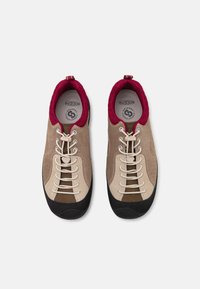 Chaussures d'escalade brun clair avec une tige en daim, un pare-pierre en caoutchouc noir et un col en mesh bordeaux. Elles possèdent des lacets blancs et des accents perforés.