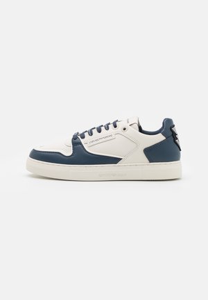 Niedriger Sneaker in Weiß und Marineblau mit Schnürverschluss, mit "Emporio Armani"-Marke an der Seite und Sohle, vor weißem Hintergrund.
