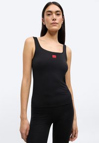 Μαύρο τοπ τύπου φανέλας κατασκευασμένο από ελαστικό ύφασμα με τετράγωνο ντεκολτέ, που διαθέτει μια μικρή κόκκινη ετικέτα με λογότυπο στ ο μπροστινό μέρος. Λείο ύφασμα και εφαρμοστό σχέδιο.