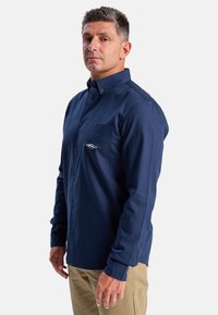 Marineblauwe, lange mouwen overhemd met knoopsluiting, gemaakt van katoen, met een borstzak met geborduurd logo en een standaard kraag.