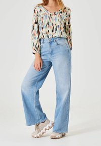 Blusa multicolor con un patrón de zigzag, mangas largas y escote en V. Jeans de pierna ancha color azul claro, con bolsillos frontales y un acabado descolorido. Zapatillas beige.