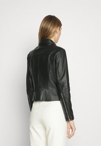 Svart skinnjacka med en figursydd siluett, vinklade sömmar och dragkedjeslutningar vid ärmarna. Slät textur och klassisk design med spetsig krage.