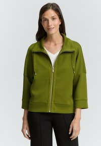 Veste zippée verte avec un col haut, des manches longues et deux poches latérales. Tissu doux avec une texture lisse et des détails de conception simples.