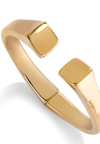 Pulsera de brazalete de oro con un acabado liso y brillante, que presenta extremos cuadrados y un diseño abierto y moderno. Ligera y con una textura pulida.