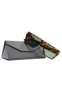 Occhiali da sole tartarugati con lenti verdi, inclinati leggermente, poggiati su un astuccio nero triangolare testurizzato con chiusura a patta.