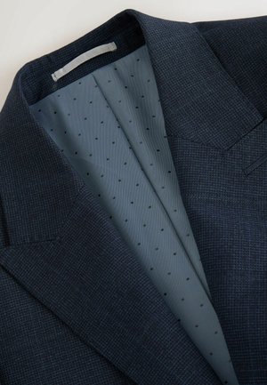 Blazer de un marin închis, confecționat dintr-un material texturat. Interiorul are o căptușeală de un albastru deschis, căptușită cu buline negre mici. Umeri structurati remarcabili.