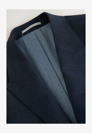 Dunkelblazer in Navy mit einer strukturierten Textur. Das Innenfutter ist hellblau mit kleinen schwarzen Punkten. Auffällige strukturierte Schultern.