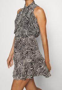 Robe sans manches à imprimé zèbre noir et blanc cassé avec un col montant, une taille élastique et un ourlet en volants superposés. Texturé en tissu léger.