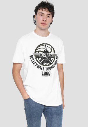 Weißes Baumwoll-T-Shirt mit einem schwarzen Grafikdruck, der "TOP GUN", ein Volleyballdesign und den Text "1986 FIGHTERTOWN USA" zeigt. Kurze Ärmel, Rundhalsausschnitt.